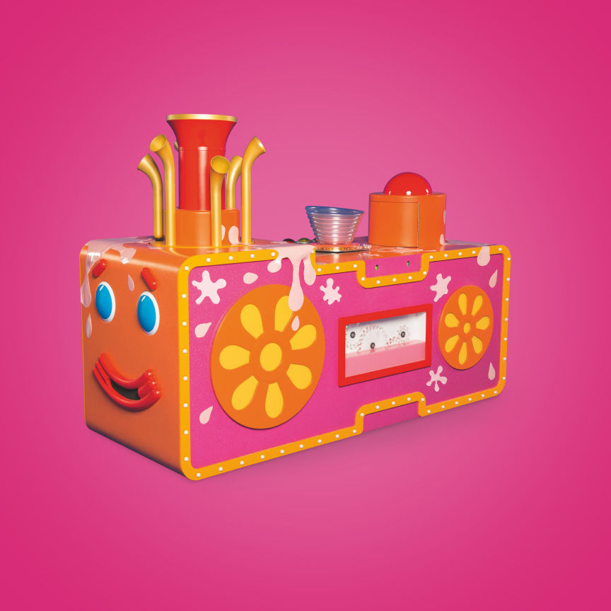 A pink and orange rectangular object with blue eyes, red mouth and yellow flowers on it.