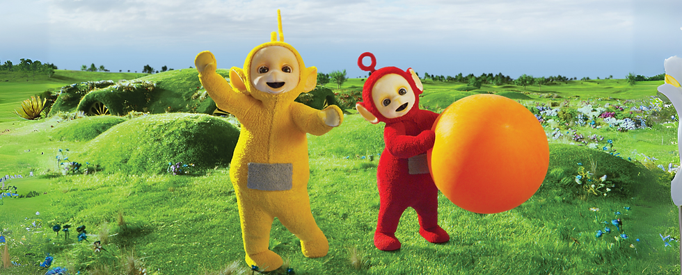 Laa-Laa, the yellow Teletubby, and Po, the red Teletubby standing in the grass. Po is holding a large orange ball.