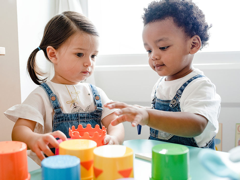 two children in overalls playing with cups at a table